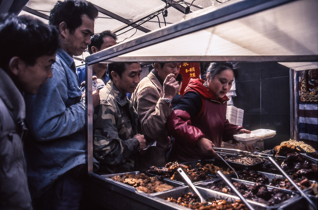 #24 Street food hustle. The lady on the right is working the food stand. It's lunch time so it's important to get food quick.